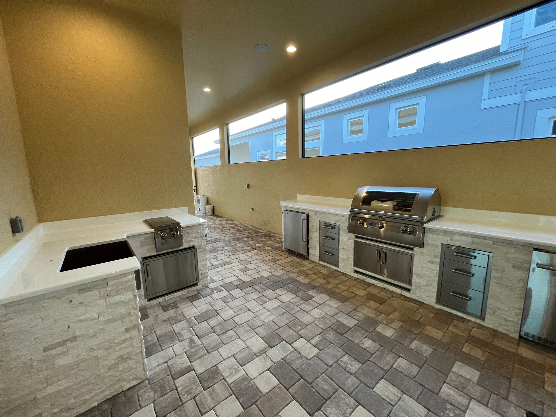 Outdoor kitchen with grill, counters, cabinets, and brick pavers.