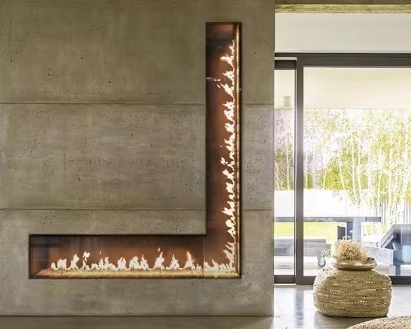 Modern, L-shaped fireplace with flames against a concrete wall. Adjacent to a large window with outdoor view.