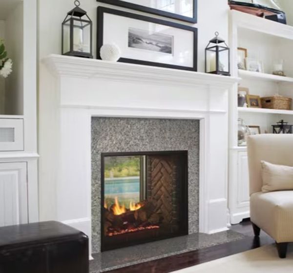 White fireplace with lit fire, flanked by cabinets, decorated with lanterns and framed art.