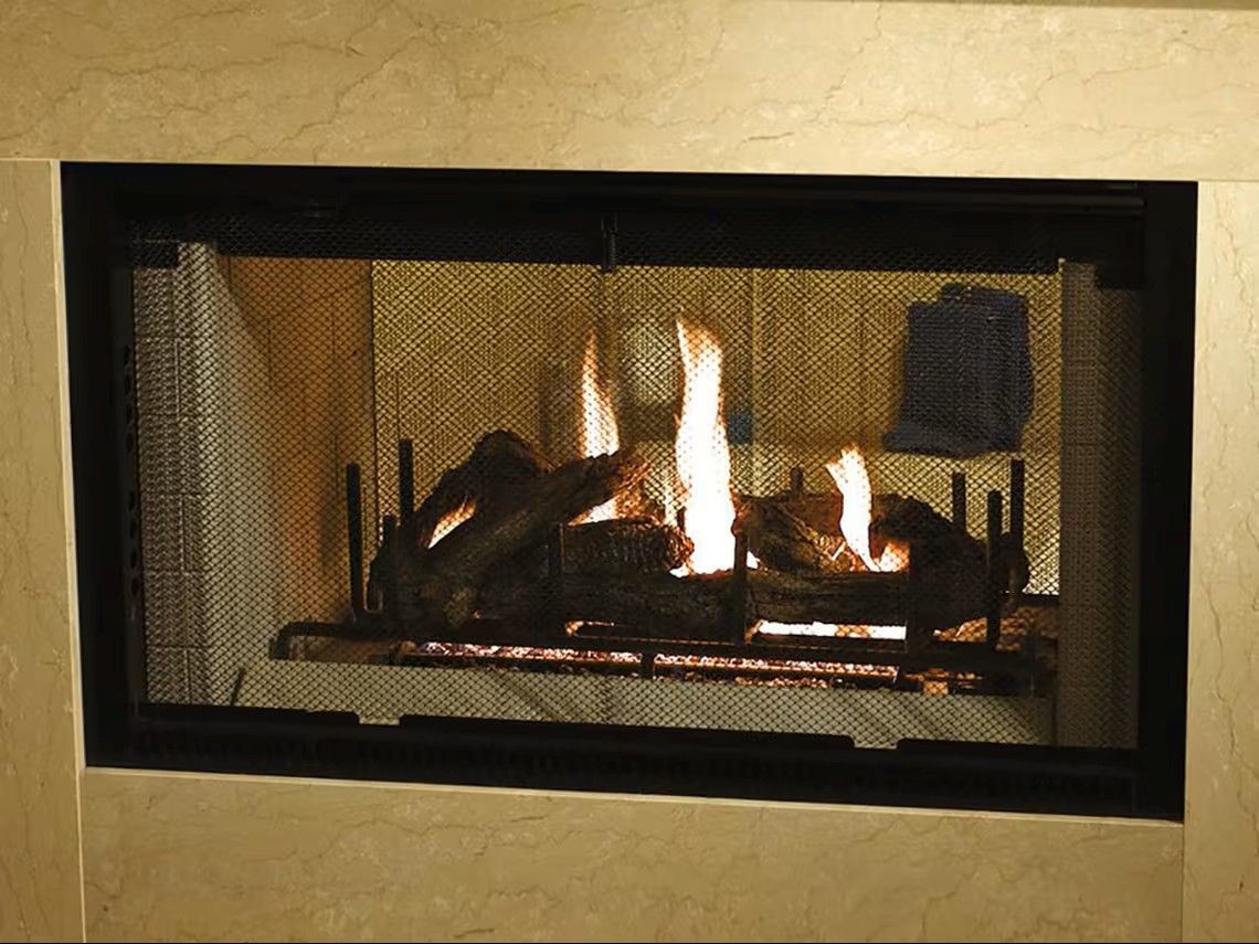 Fire burning in a fireplace behind a mesh screen; flames are yellow/orange.