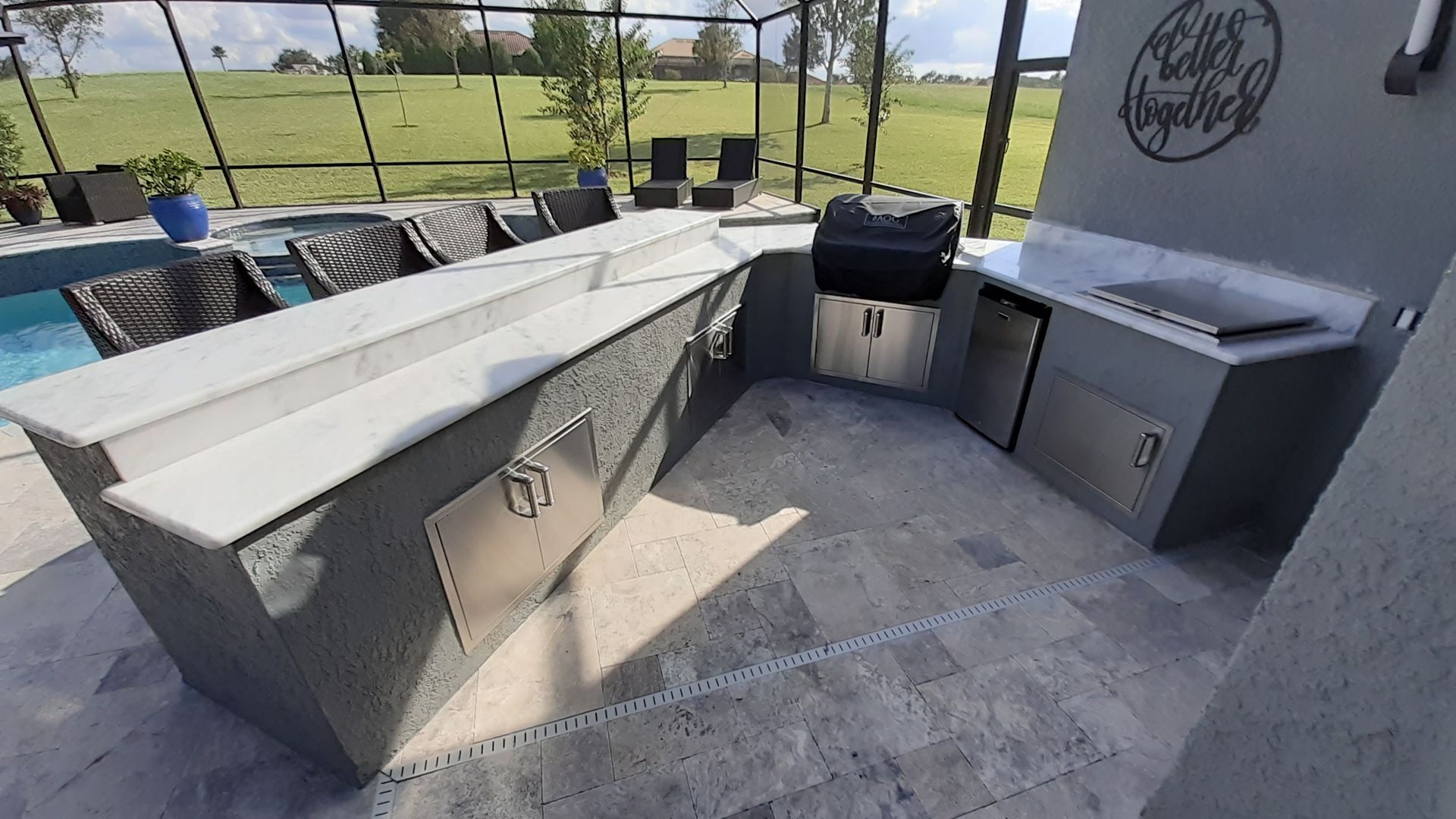 Outdoor kitchen with gray countertops, stainless steel appliances, and a pool in the background.