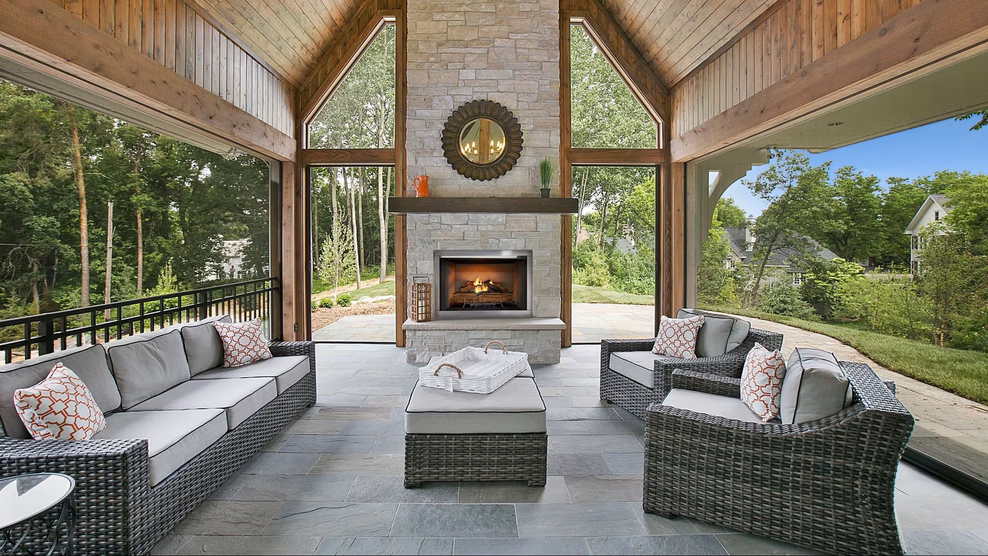 Outdoor living area with stone fireplace, sofas, and natural wood ceiling.