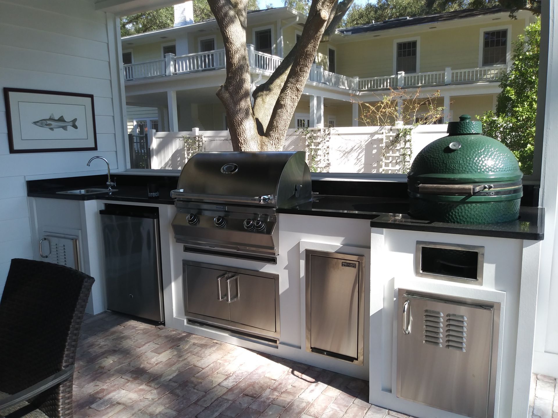 Outdoor kitchen with grill, Big Green Egg, sink, and stainless steel appliances; patio setting.
