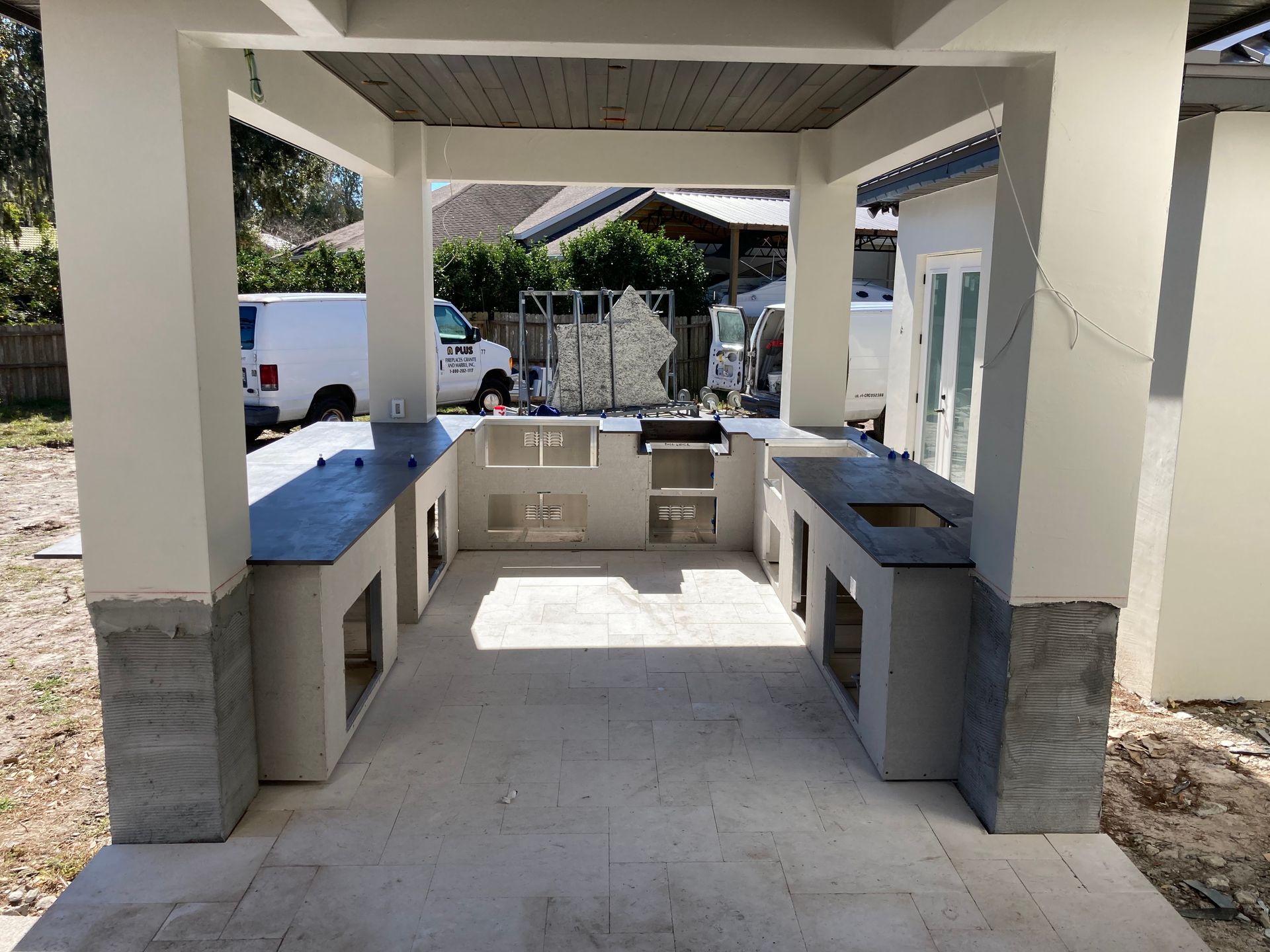 Outdoor kitchen with gray countertops and white pillars under a covered patio.