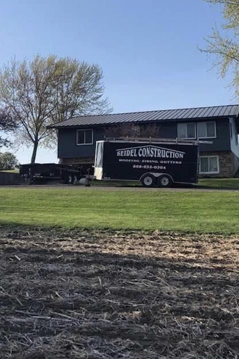 Black construction trailer parked in front of a house with trees and a field in the foreground