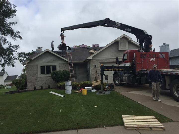 Construction crane lifting roof debris from a damaged suburban house, with workers and equipment nearby