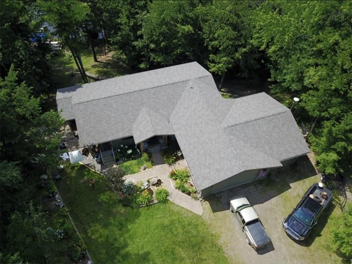 Aerial view of a house with gray roof, surrounded by trees and a driveway with two cars.