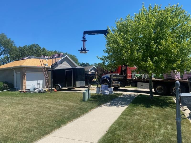 Tree service crew and crane truck working beside a suburban house with a covered roof and sidewalk.
