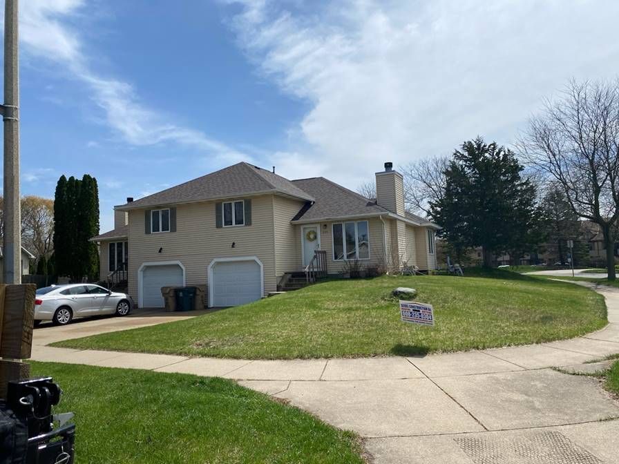 Suburban house on a corner lot with a curved driveway, garage, and a car parked outside under a blue sky