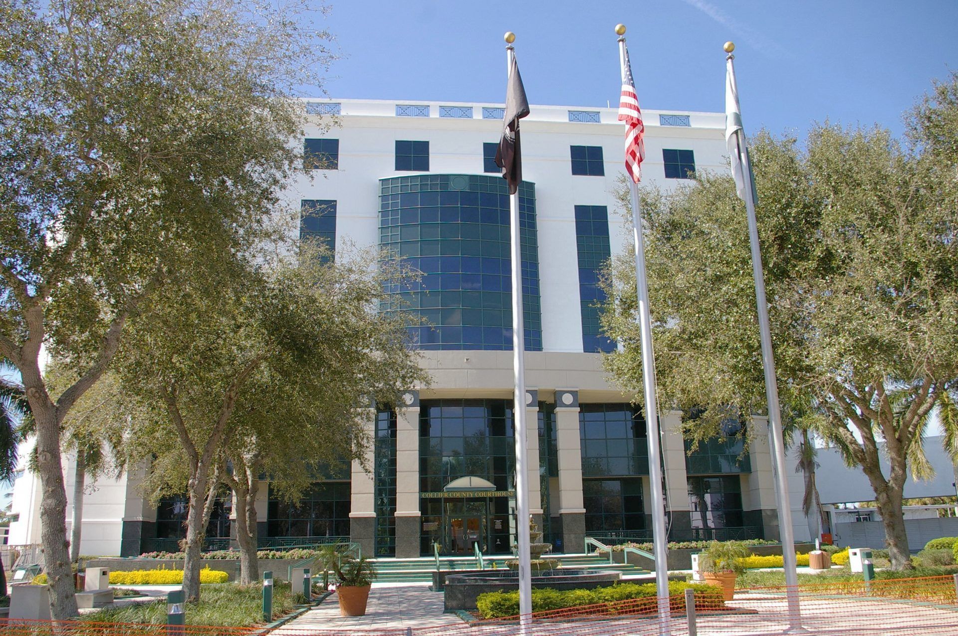 Modern white office building with glass entrance, trees, and flagpoles in front