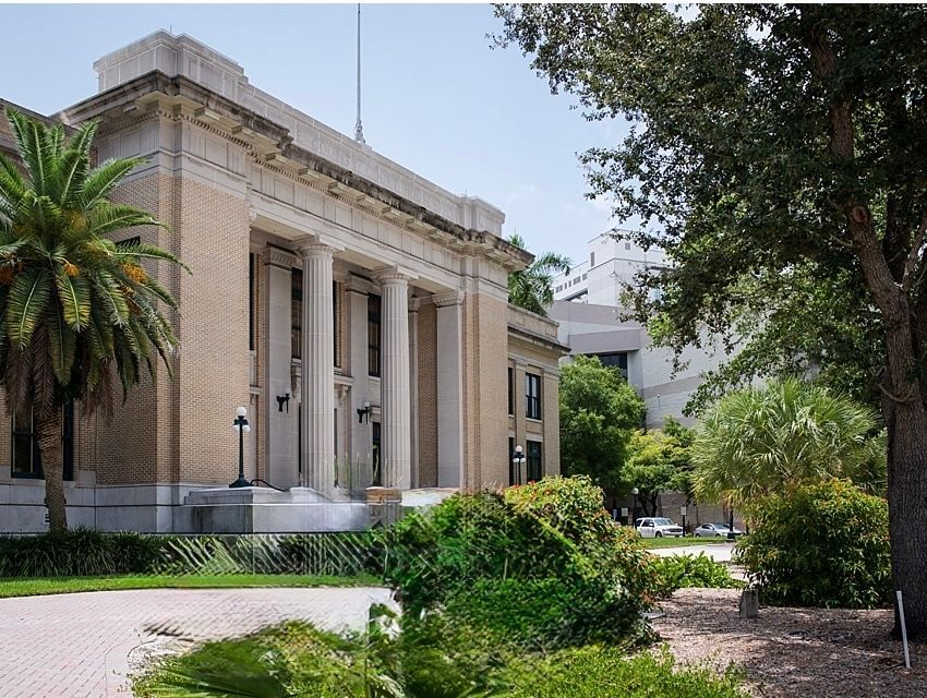 Classical stone building with columns and palm trees beside a landscaped courtyard