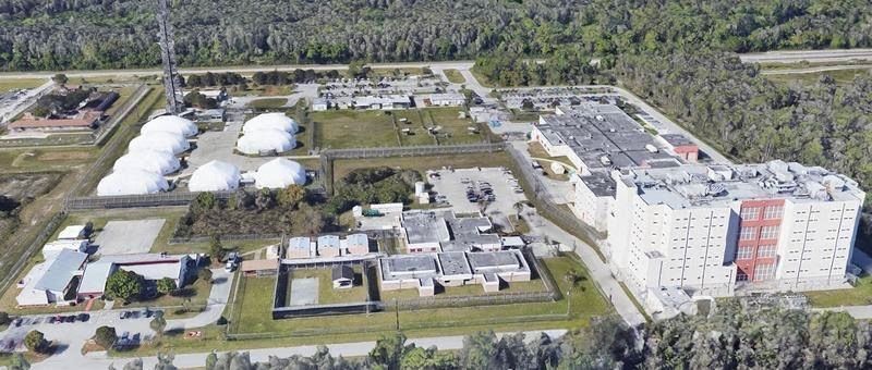 Aerial view of a large industrial complex with tanks, buildings, and forest surrounding it