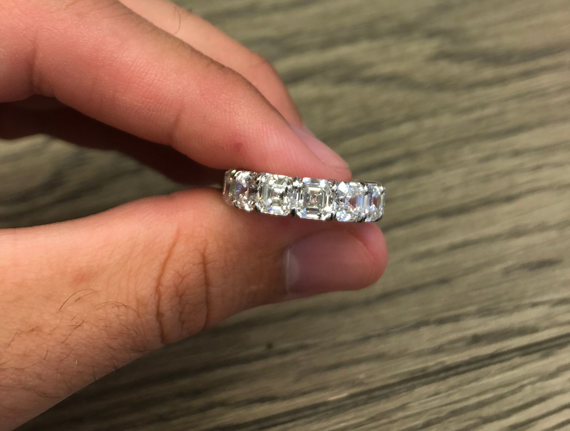 Hand holding a silver ring with many clear square-cut stones, close-up.