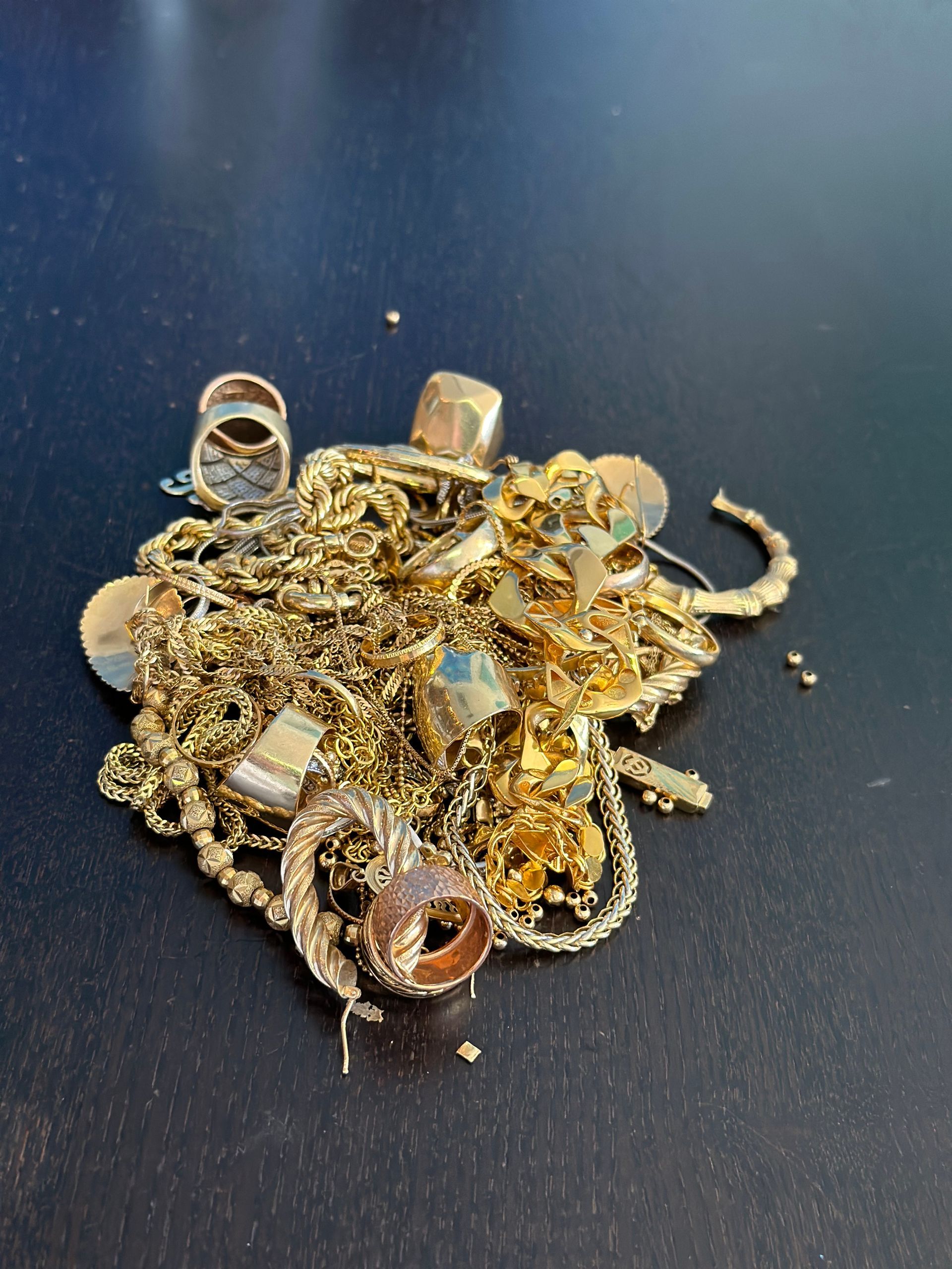 Pile of gold jewelry: rings, chains, and other items on a dark surface.
