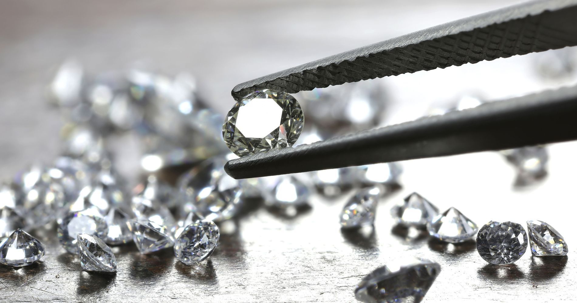 Tweezers holding a diamond; other diamonds scattered on a surface.