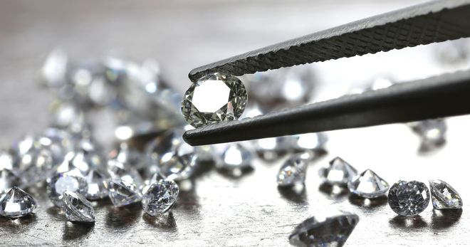 Tweezers holding a diamond; other diamonds scattered on a surface.