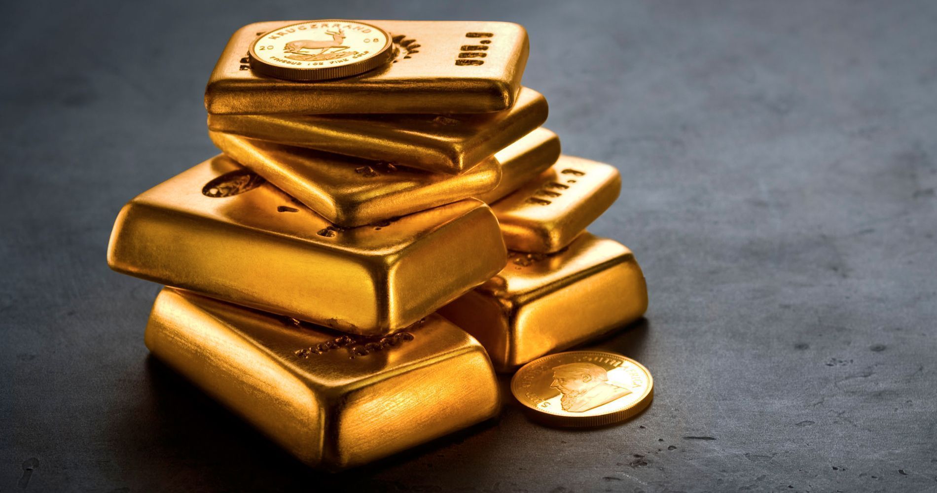 Gold bars and coins stacked on a dark surface.