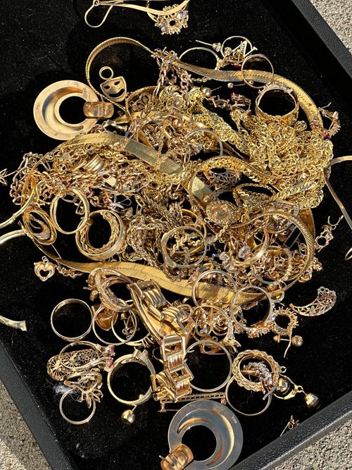 Pile of gold jewelry in a black tray, including rings, necklaces, and earrings.