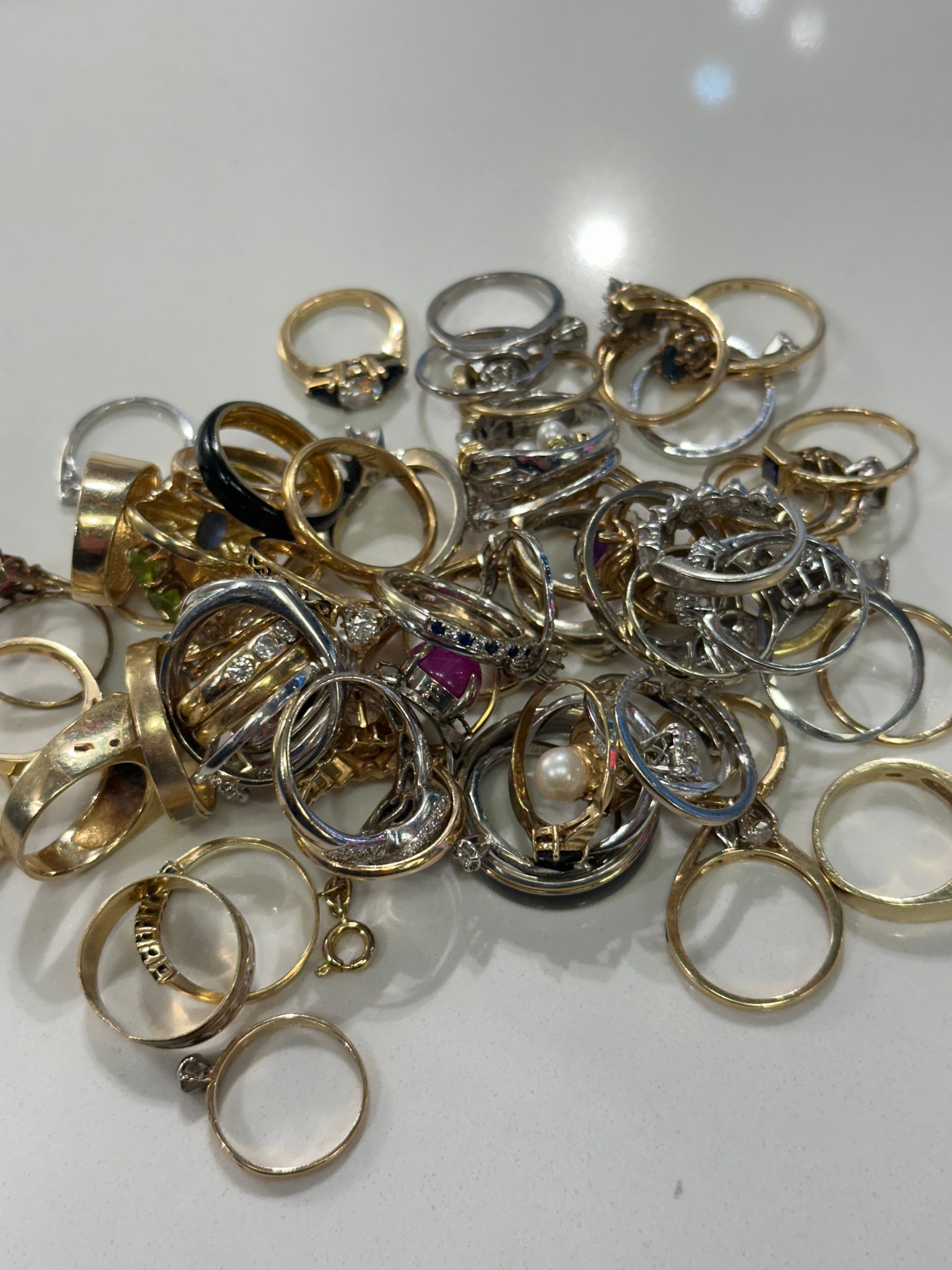 Pile of gold and silver rings, some with gemstones, on a white surface.