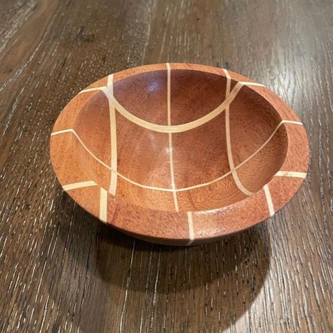 Wooden bowl with a reddish-brown hue and white inlay design on a wooden table.