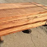 A stack of reddish-brown wood planks, tightly bound, resting on a concrete surface.