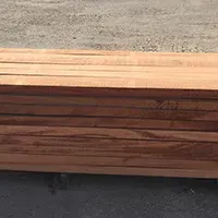 Stack of reddish-brown wooden boards lying on a gray surface, likely outdoors.