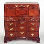 A mahogany secretary desk with a sloped top, drawers, and shell carvings. It has brass hardware and is set against a white background.