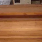 Close-up of wooden steps, showing the grain and color of the wood. A wall with a white cabinet is in the background.