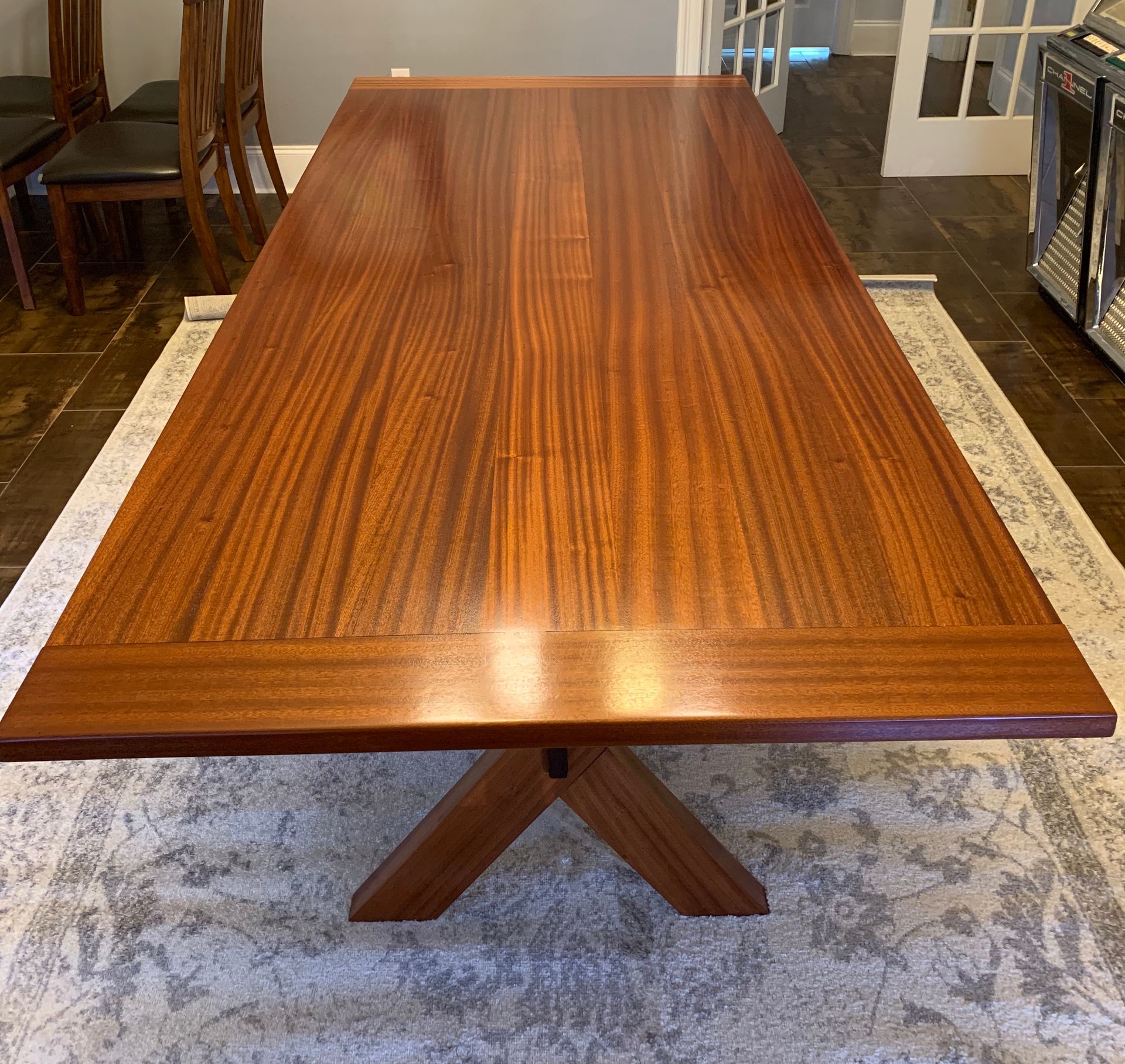 Mahogany dining table with cross base on patterned rug.