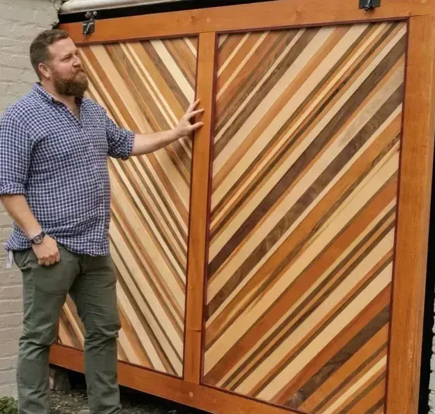 Man standing next to two large, wooden sliding doors with diagonal striped patterns. The doors are in a brown wooden frame.