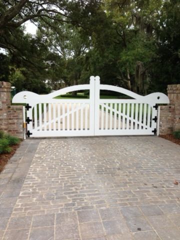 White wooden gates on a brick driveway. The gates are arched and flanked by brick pillars.