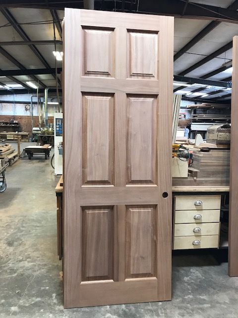 Wooden six-panel door in a workshop setting; natural wood tone, unpainted.