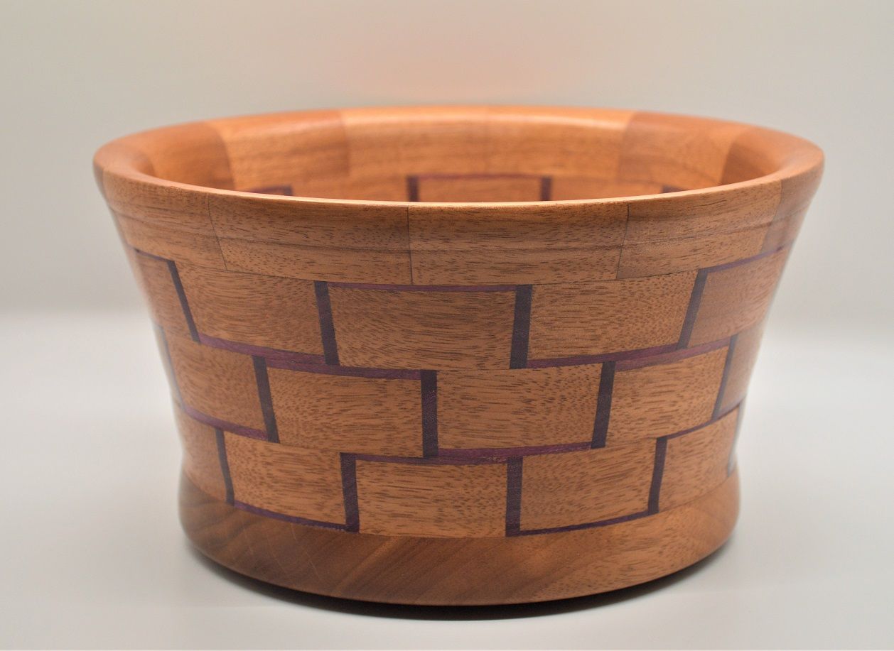 A wooden bowl with a geometric brickwork pattern, featuring brown and purple accents, set against a white background.