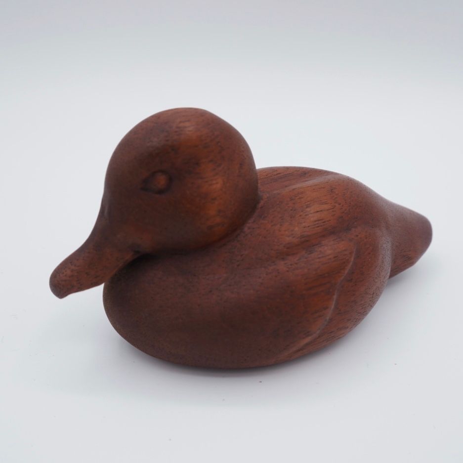 Wooden duck figurine, brown, with a rounded body and outstretched beak, against a white background.