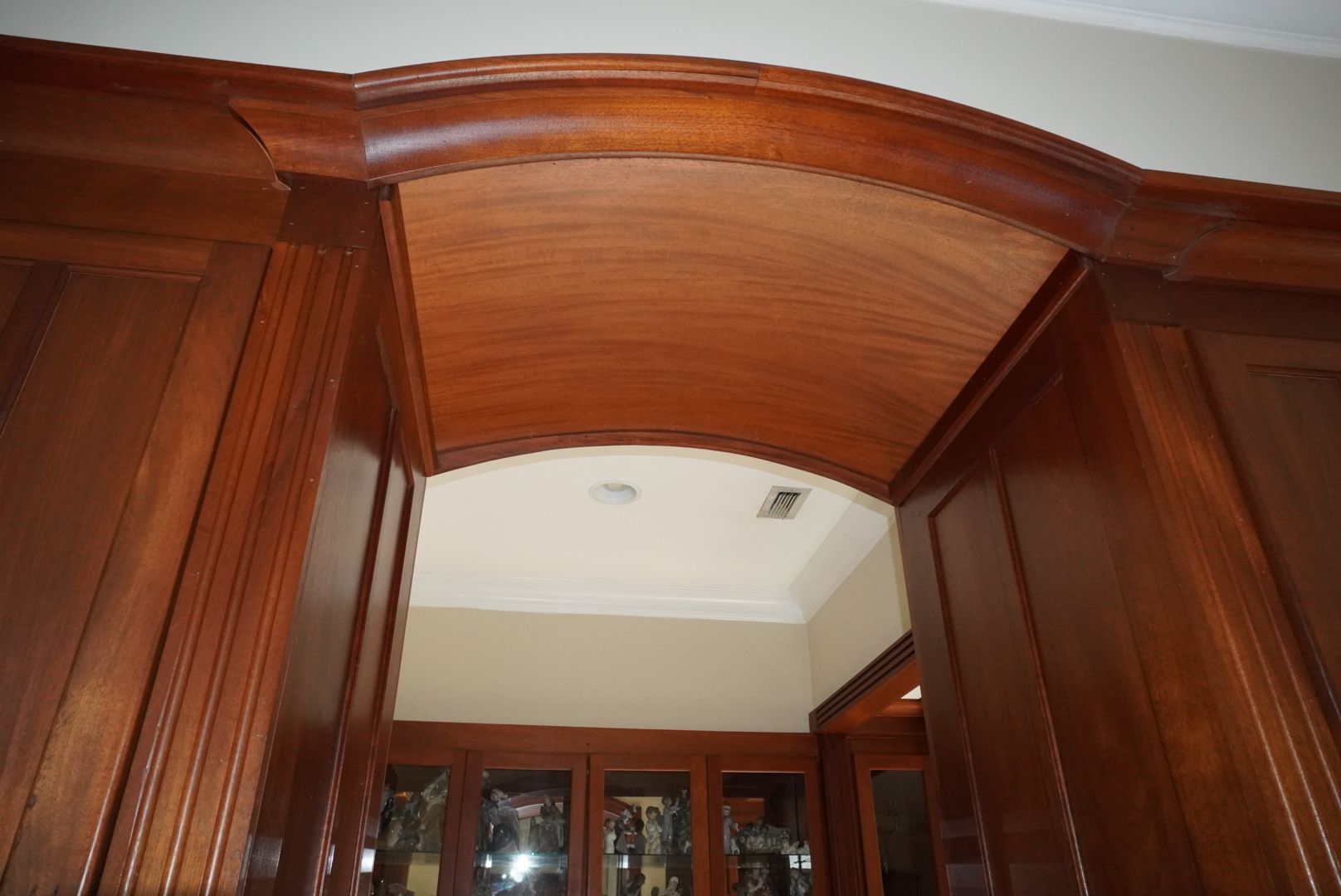 Wooden arched entryway with dark brown trim. The entryway leads to a room with white ceiling and beige walls.