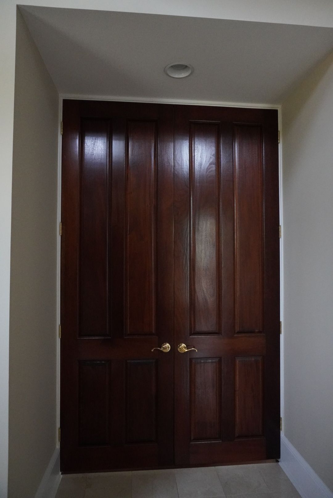 Dark wood double doors with gold handles in a beige hallway. A recessed light is above.