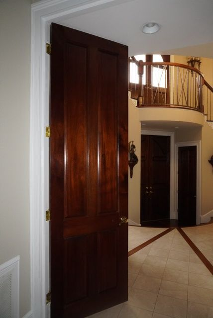 A dark wood door is slightly open, revealing a bright foyer with a curved staircase and tile floor.