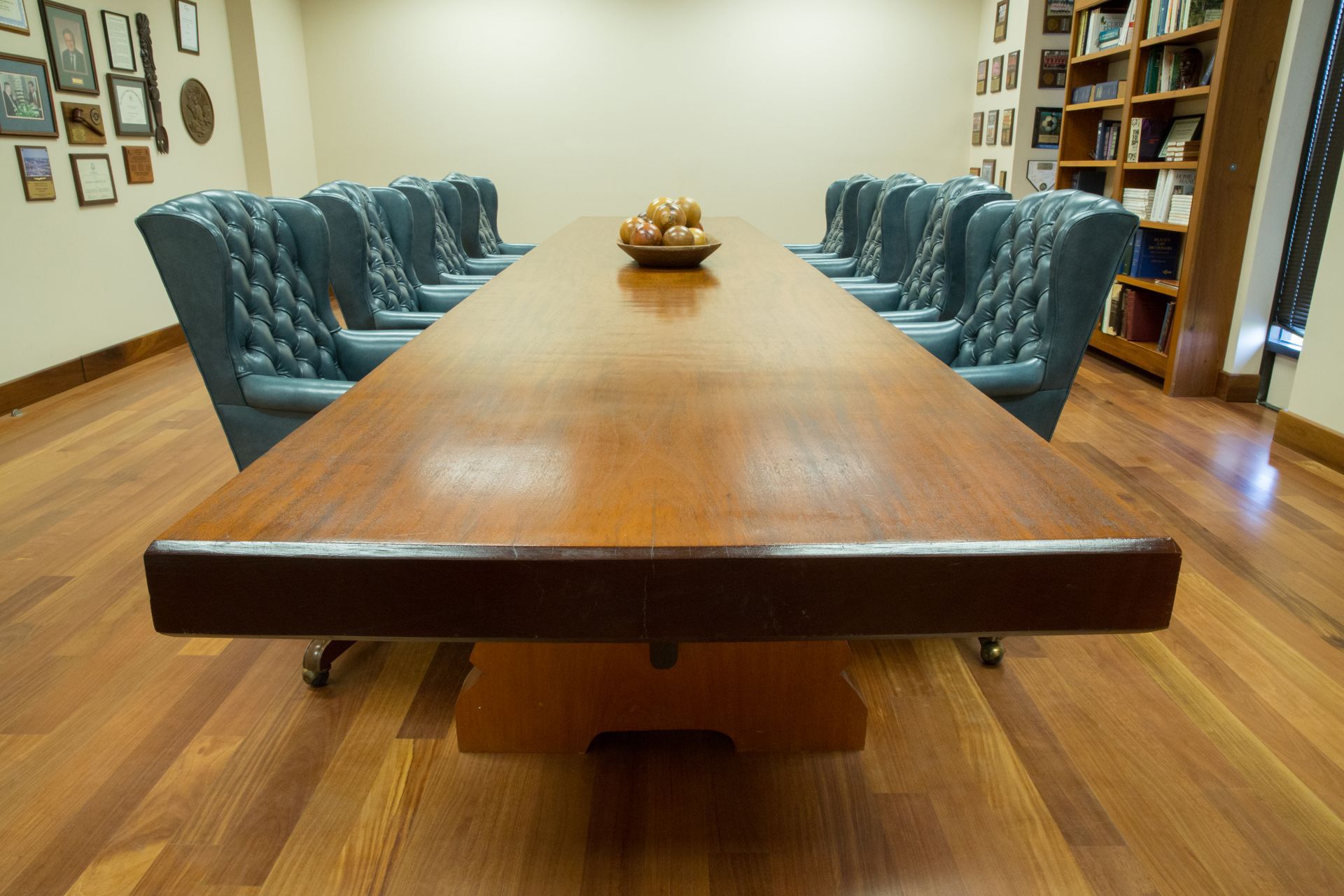 Conference room with a long, wooden table and blue chairs, fruit bowl in the center, hardwood floors.