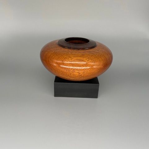 A wooden, orb-shaped art piece with a dark interior and glossy, orange exterior sits on a black block.