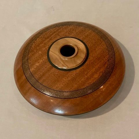 A round, wooden bowl with a light wood center and a darker, patterned rim.