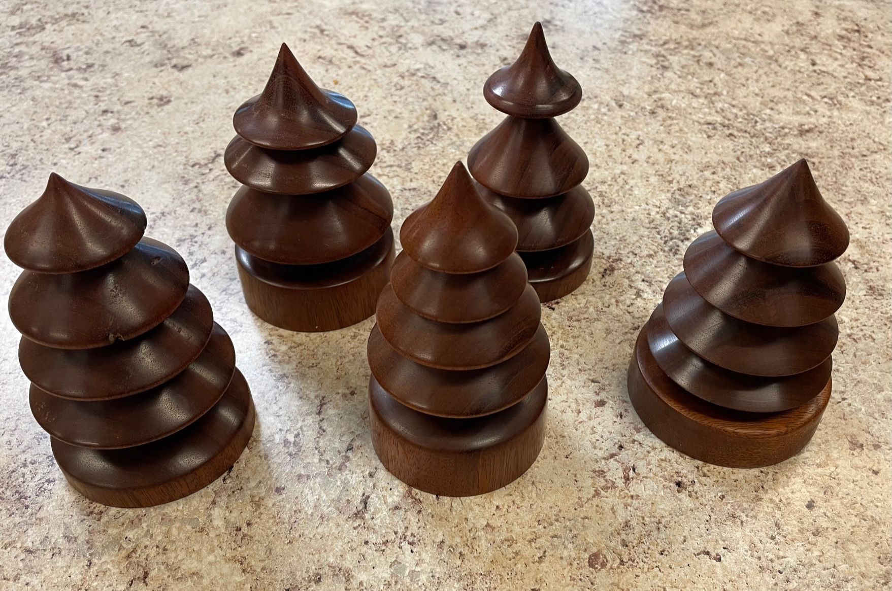 Five dark chocolate tree-shaped desserts with layered, rounded sections and pointed tops on a speckled surface.