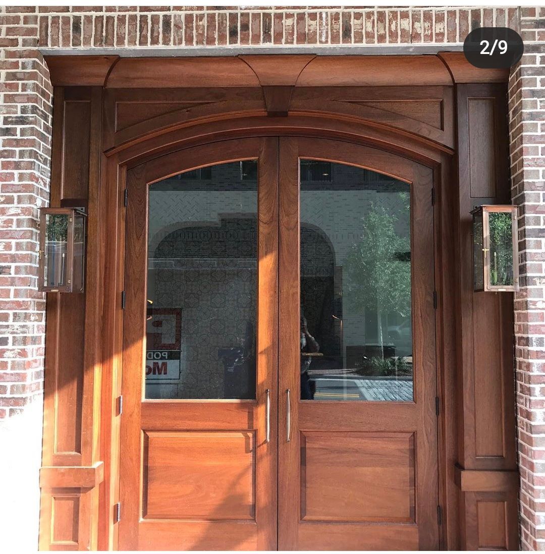 Wooden double doors with arched glass panels and side lights set into a brick facade.