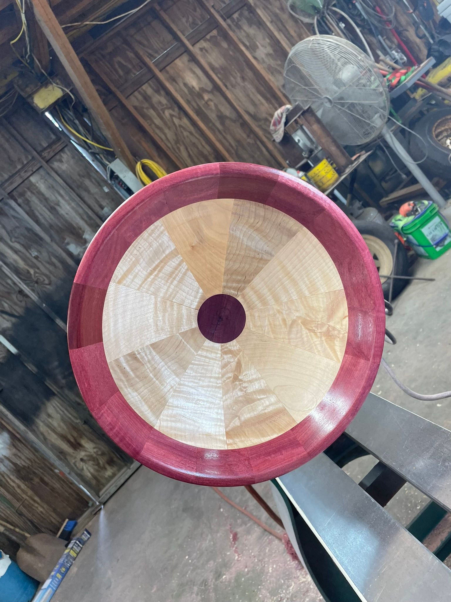 Overhead view of a wooden bowl with a purple rim, light wood center, and dark purple center. The bowl sits on a wood lathe.