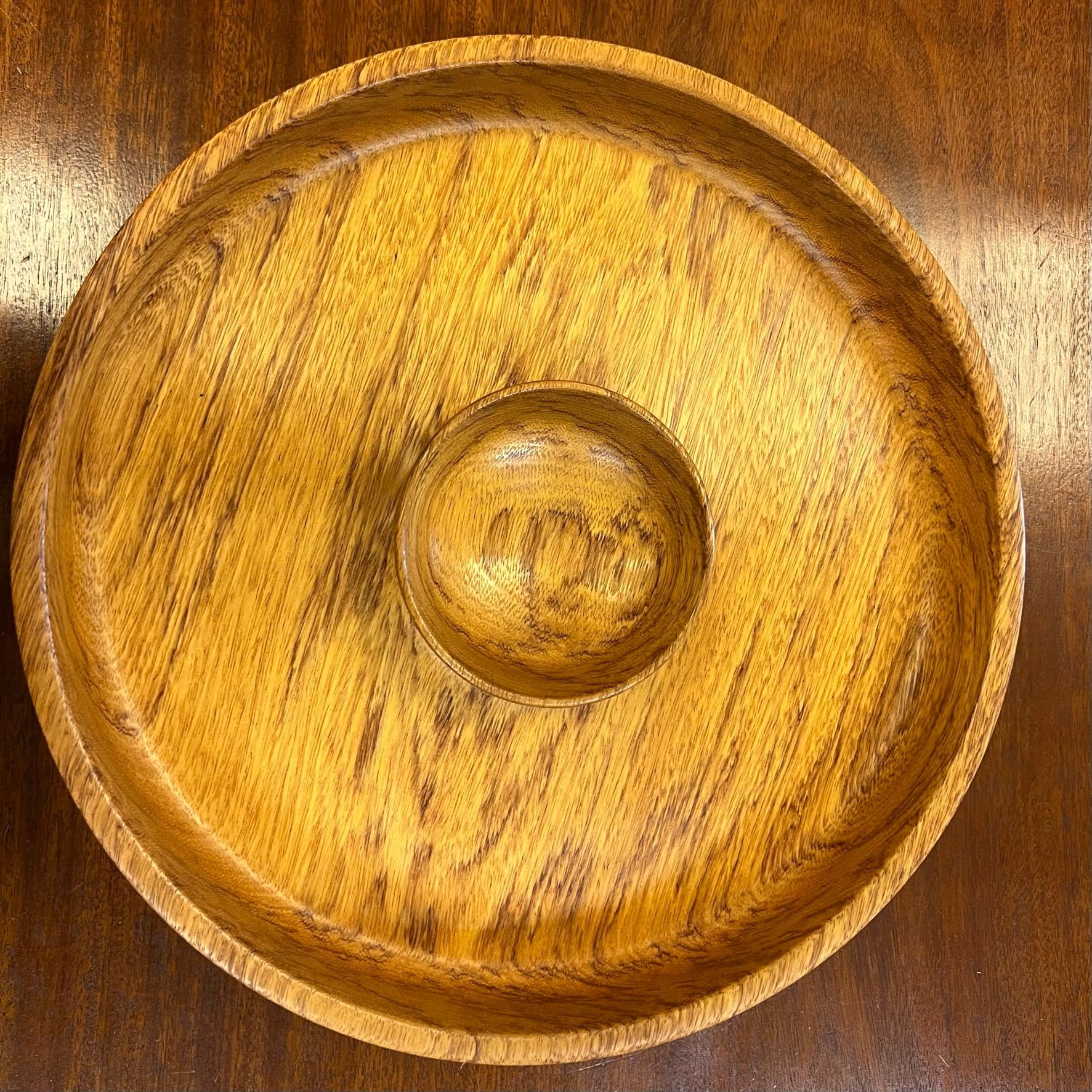 Wooden serving dish with a central dip bowl, on a dark wooden surface. Brown and gold tones.