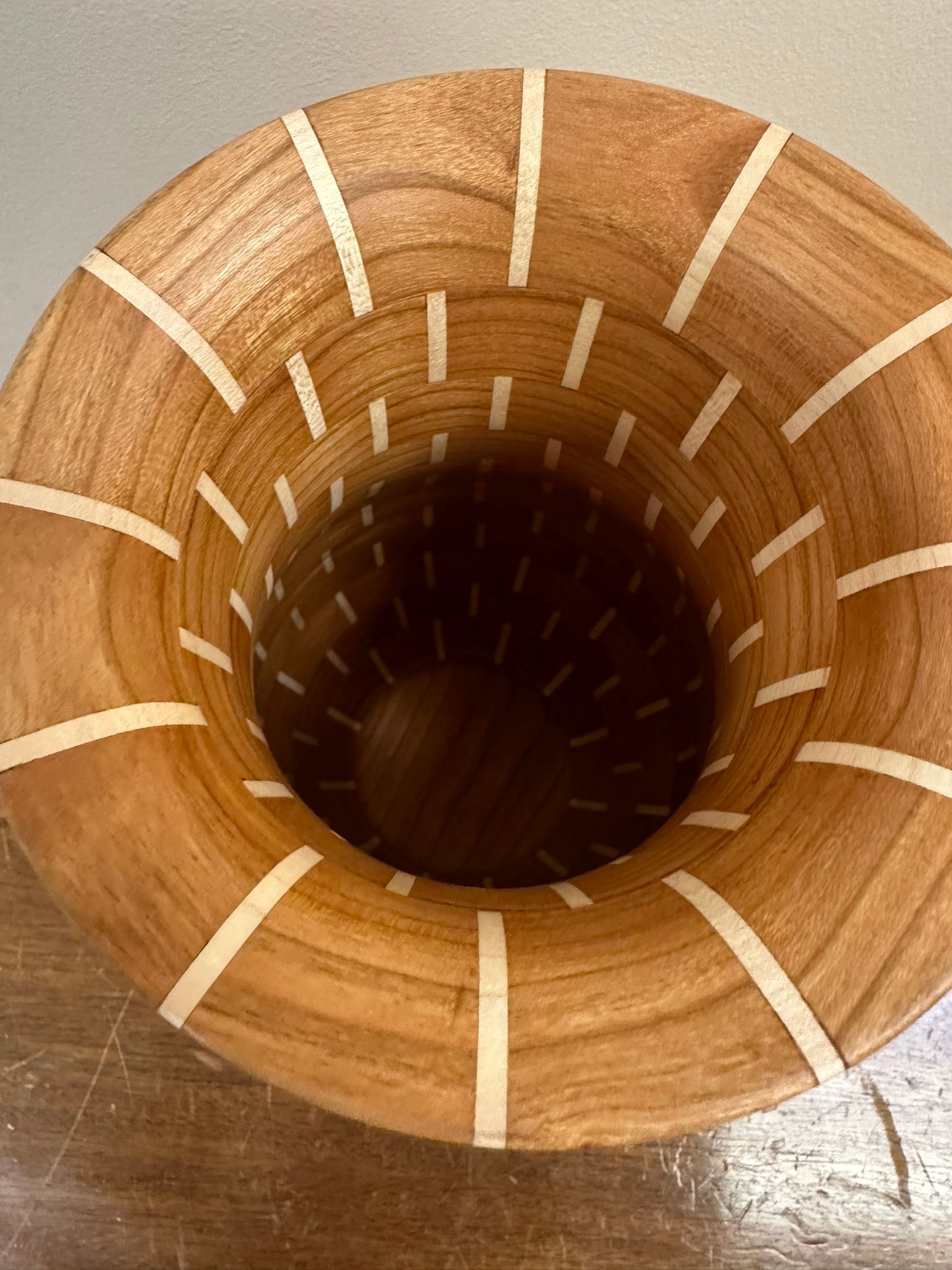 Wooden vase with light-colored inlay strips. Interior shows a dark, curved base, with a cylindrical shape opening towards the top.