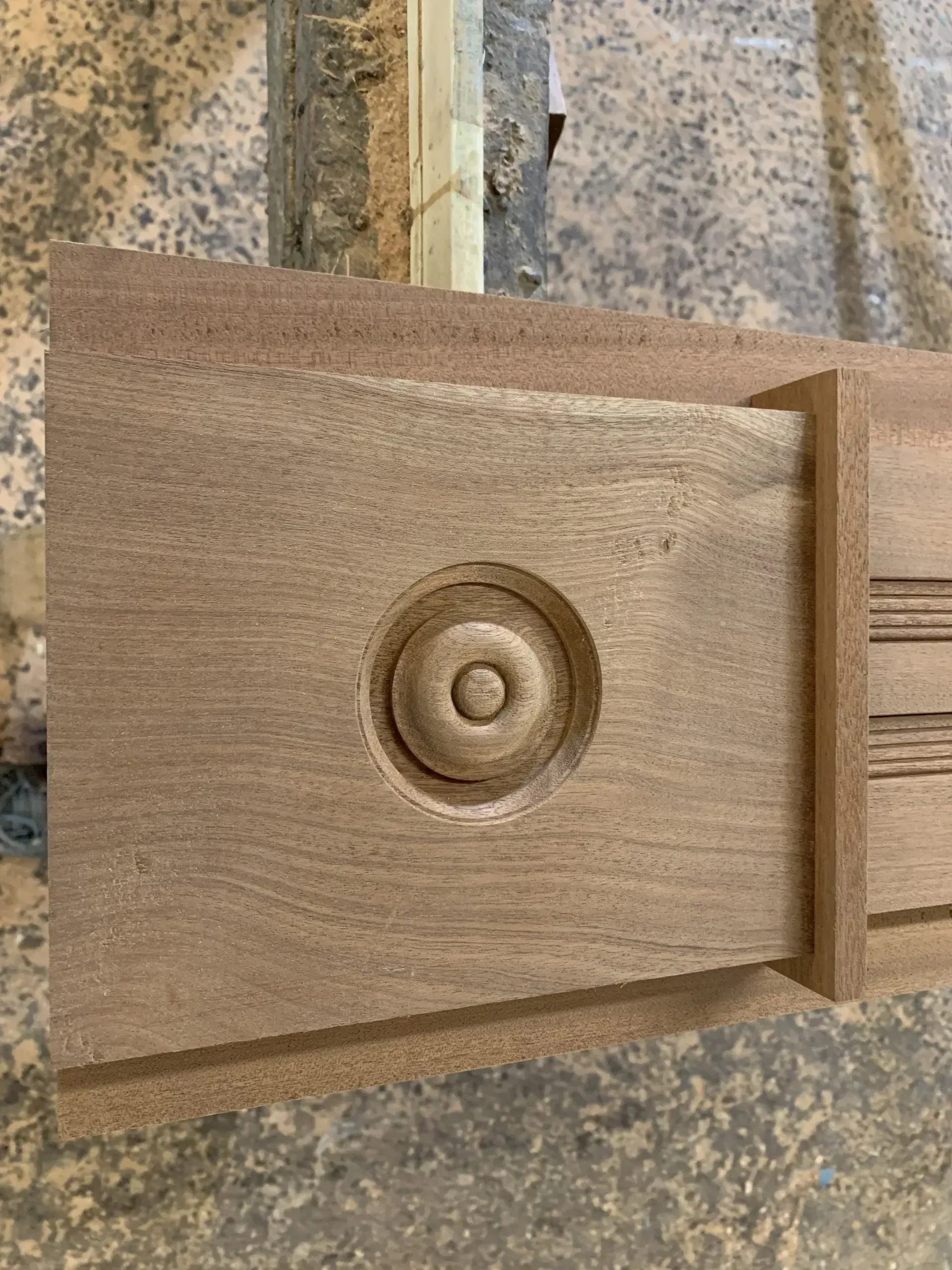 A wooden piece with a carved circular design, possibly part of a furniture component, is on a work surface.