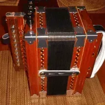 A small, brown concertina with a black bellows and silver accents, resting on a brown surface.