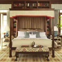 A bedroom with a large canopy bed centered in front of built-in bookshelves. The bed has light bedding, and a patterned bench sits at the foot.