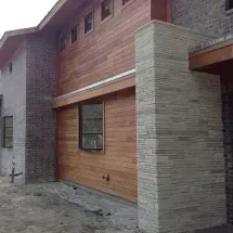 Exterior view of a modern house with wood and brick siding. The house has a flat roof and a column of light stone.