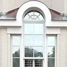 White arched window on a light-colored building with flanking windows. The window has a curved top and paneled glass.